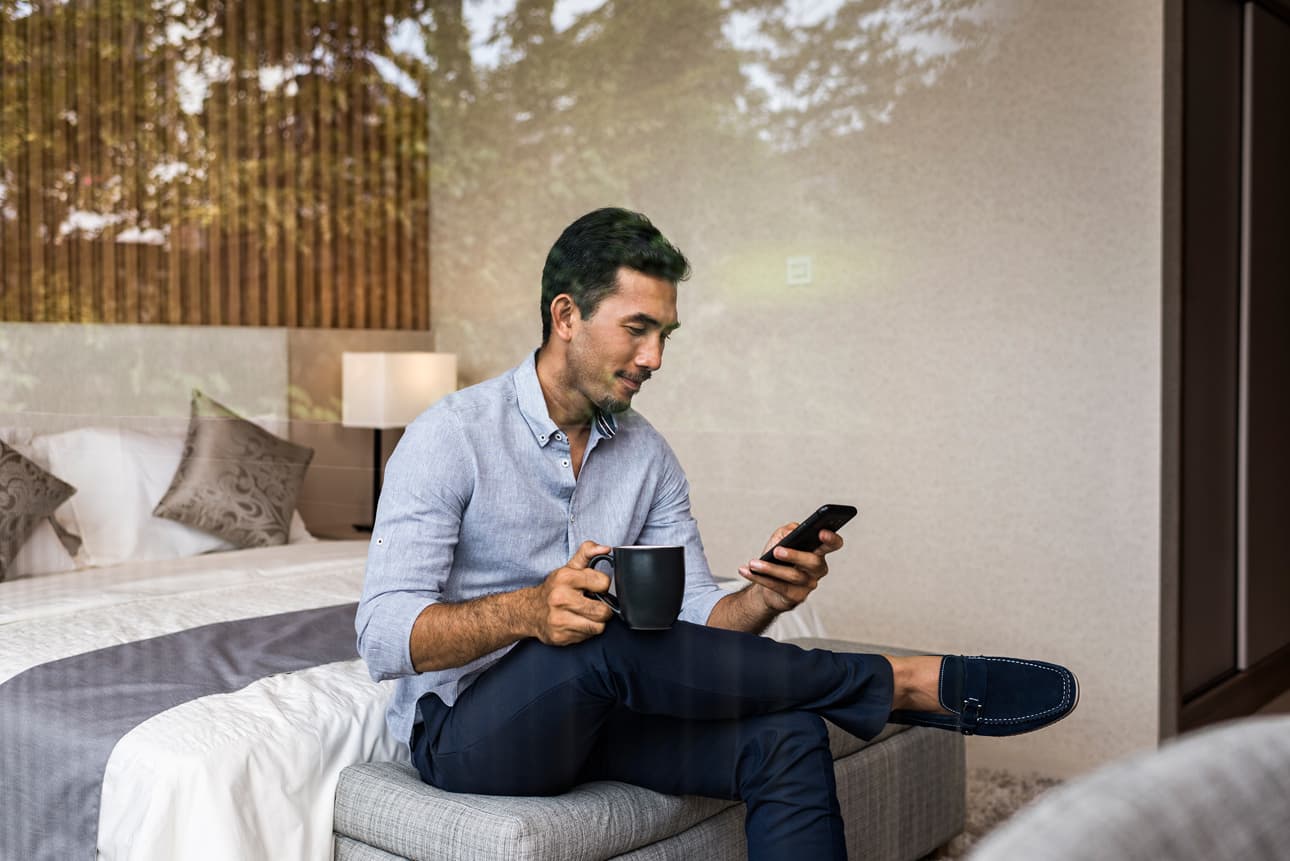 Man sitting on the end of his bed looking at mobile