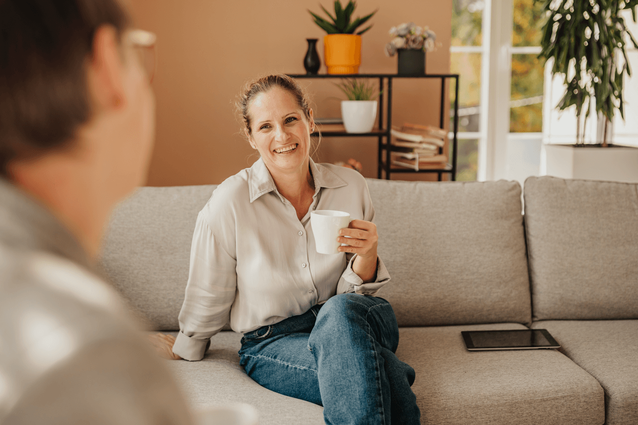 Women drinking a hot drink and smiling whilst sitting on the sofa